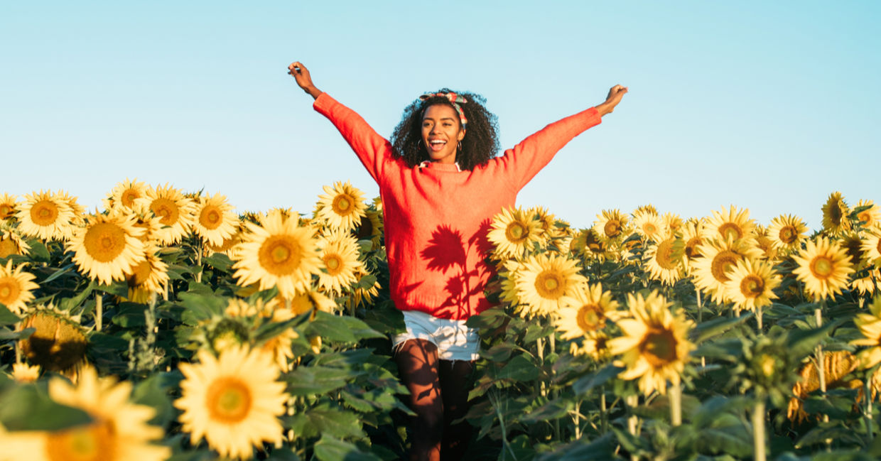 A woman joyfully walks through a field of sunflowers.