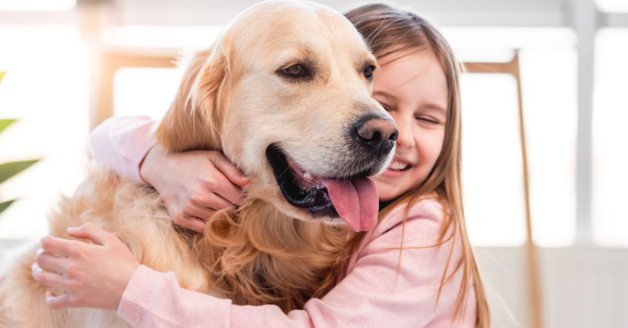 Little girl hugging her golden retriever dog and smiling.