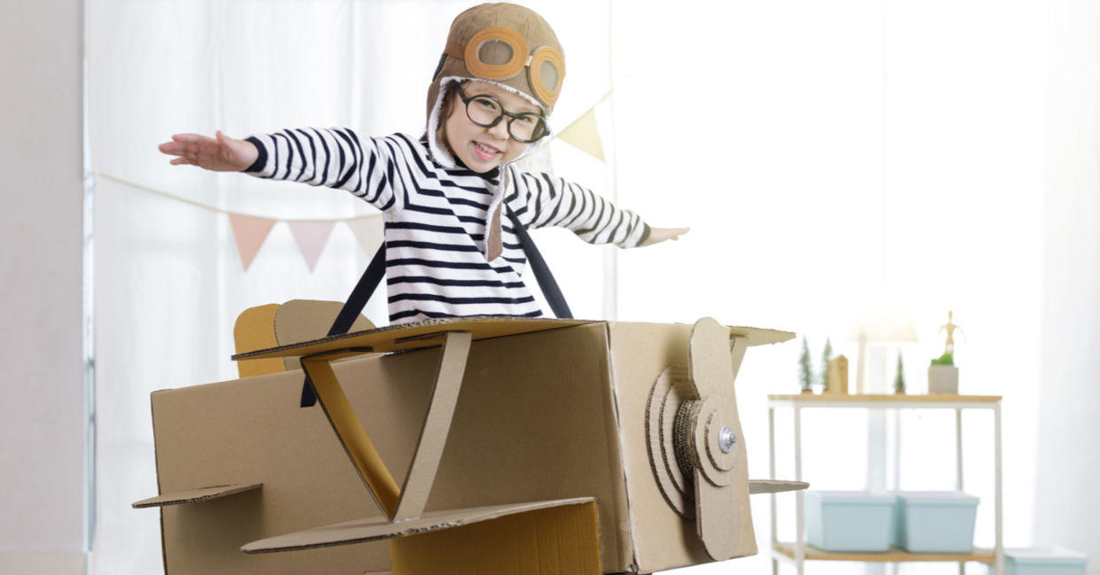 Creative little girl uses her imagination as she ‘flies’ in a cardboard box.