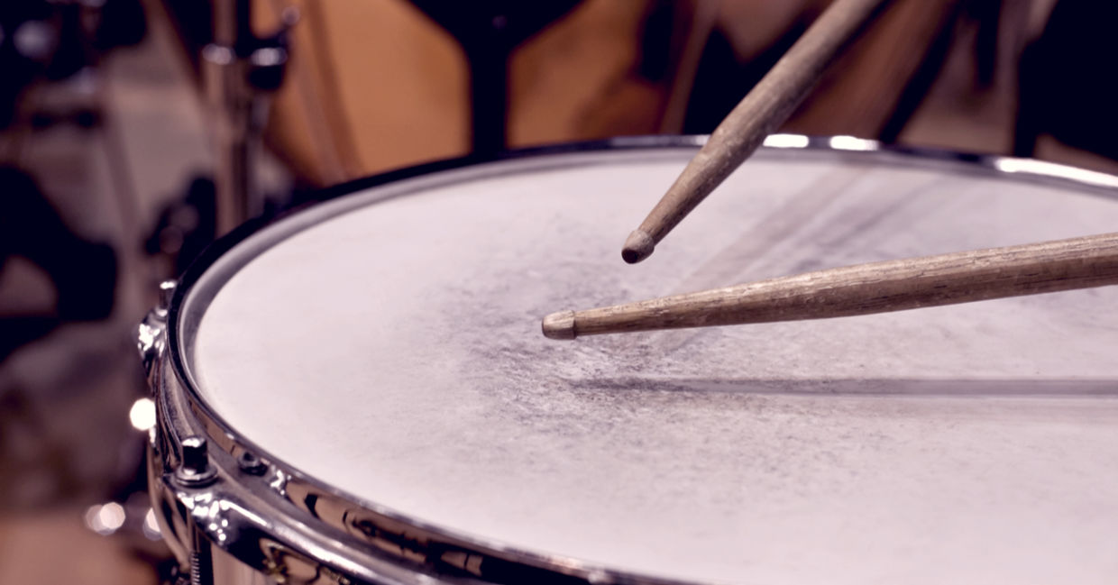 Close-up of drumsticks hitting a drum.