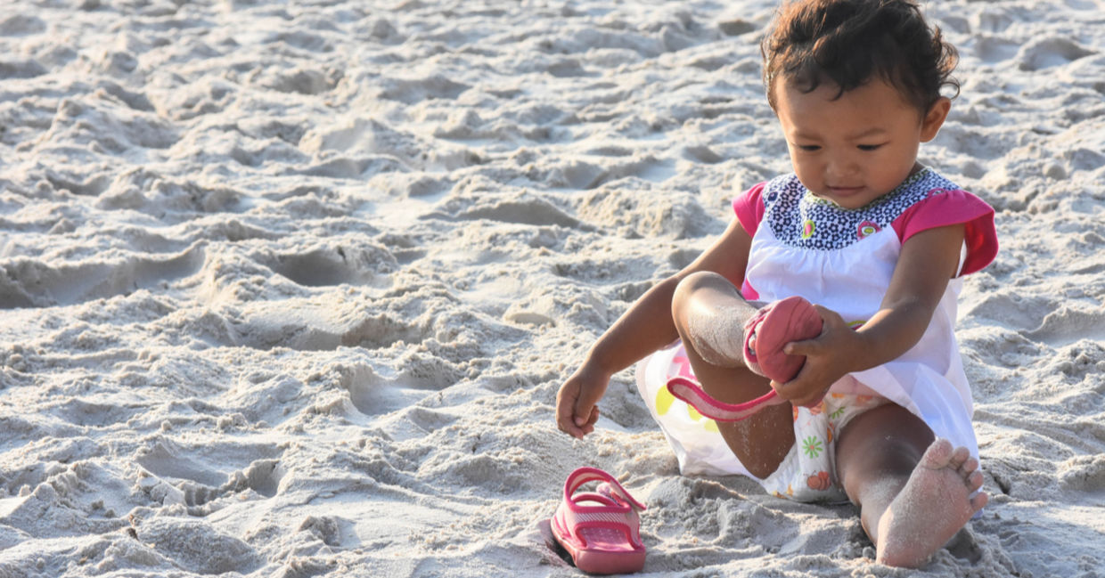 A little girl takes off her shoes while on the sand, becoming grounded.