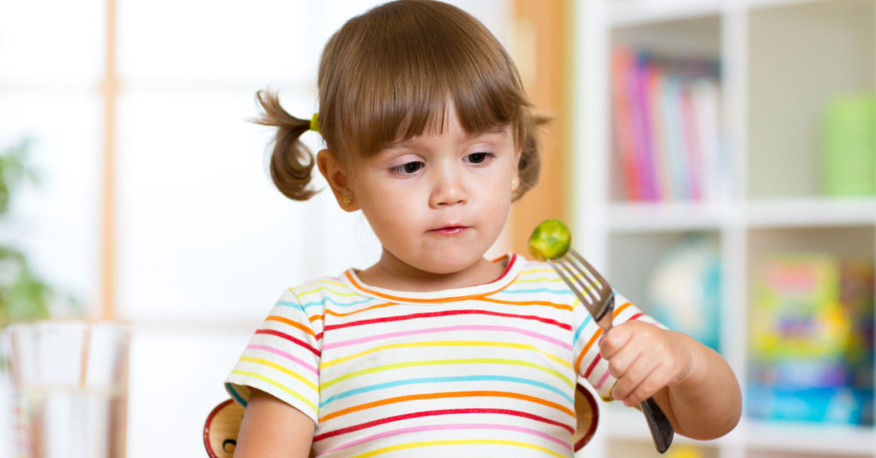 A little girl eats brussels sprouts.