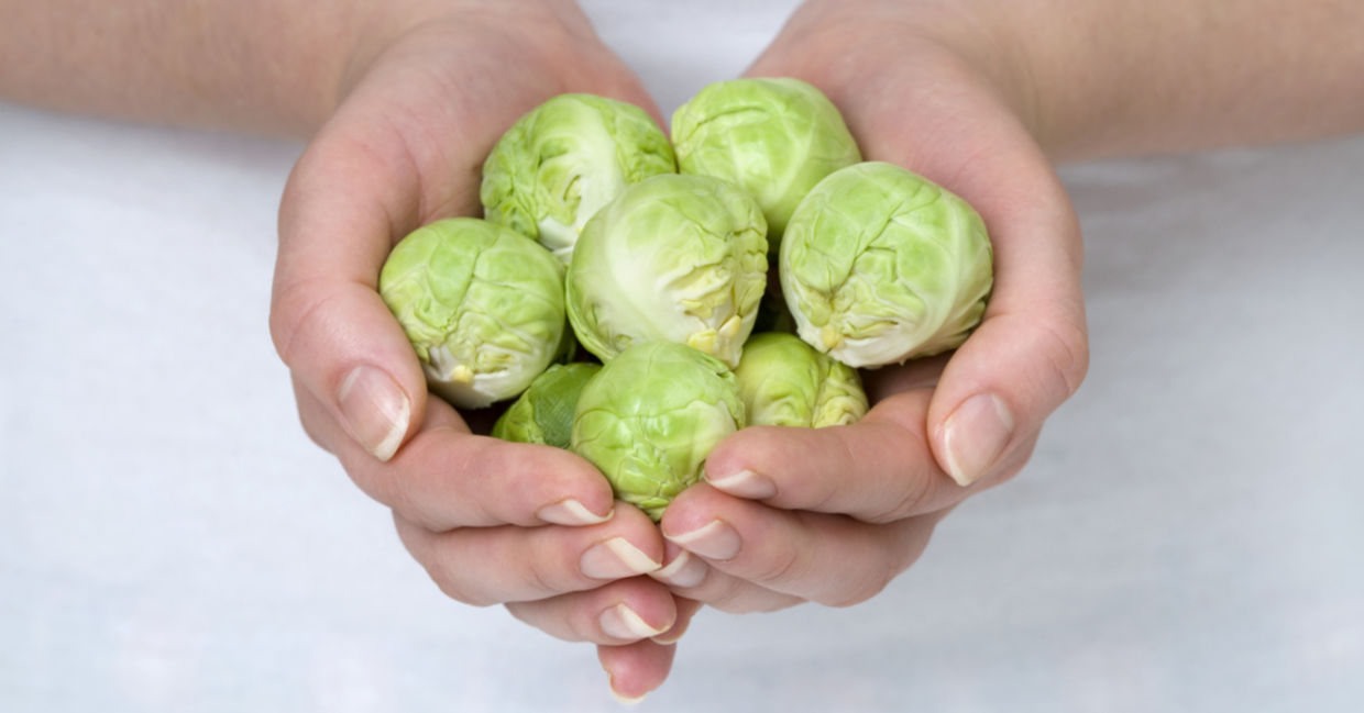 A woman with smooth hands is holding brussels sprouts.