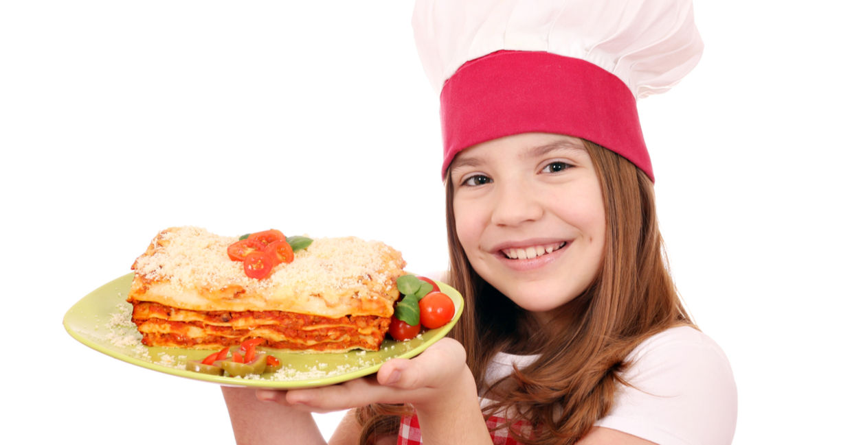A smiling young girl is holding a plate of lasagna.