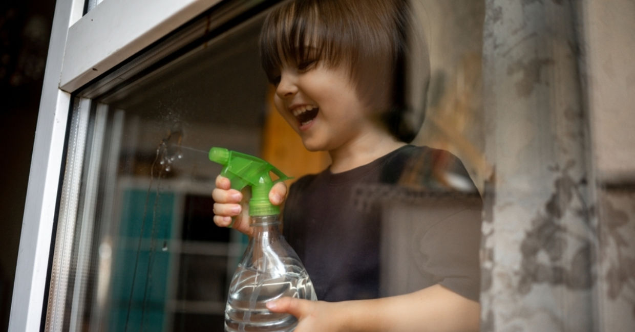 A young boy sprays glass with a DIY organic cleaner.