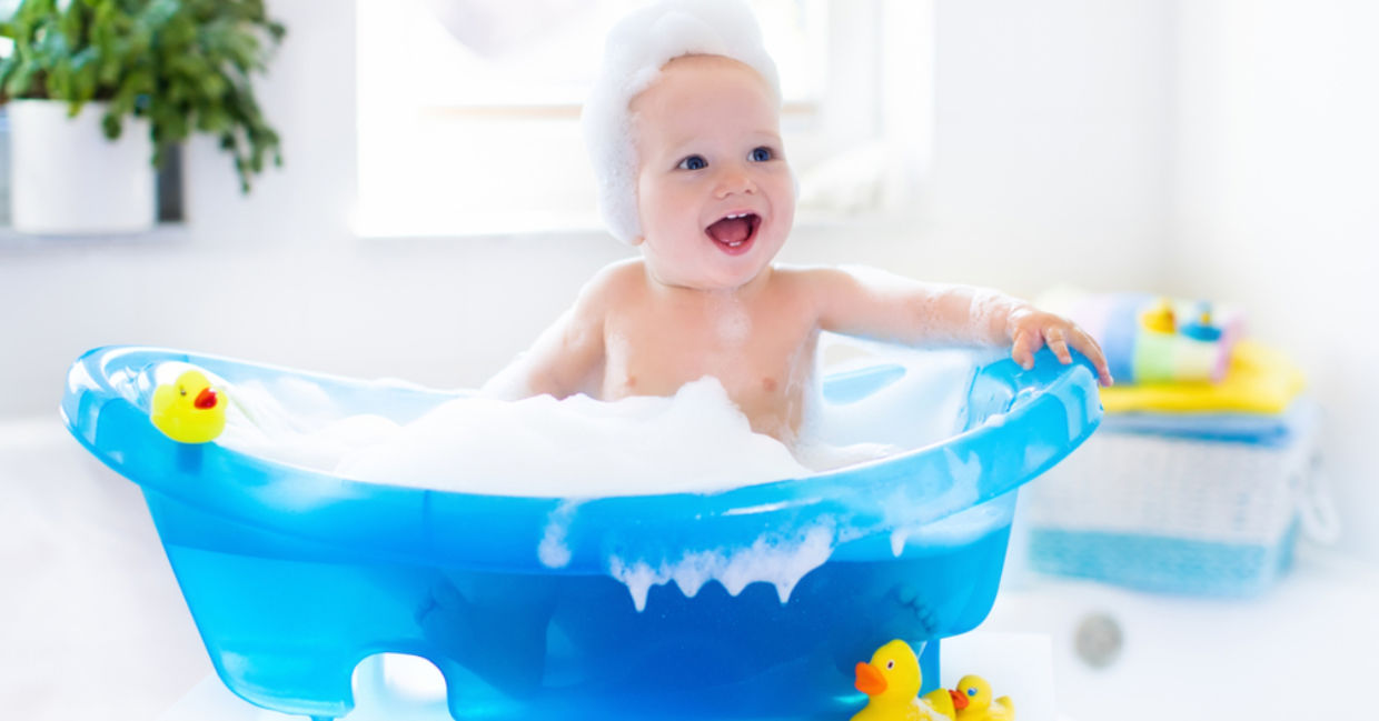 A baby with suds laughs in the tub.