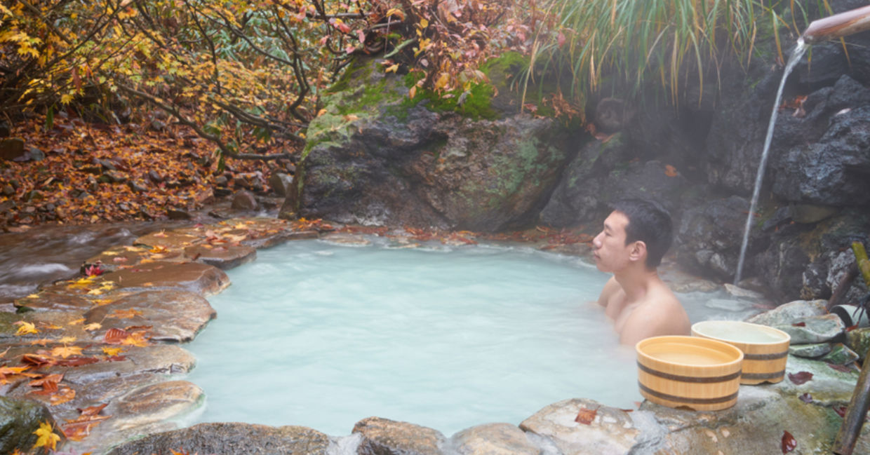 A man soaks in a mineral spring in a Japanese forest.