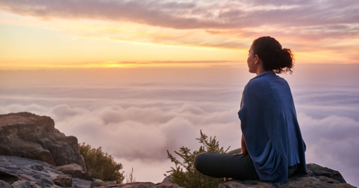 Woman sitting on a mountain top peacefully gazing at clouds