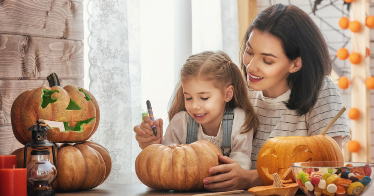 A mother carves a pumpkin for Halloween with her young daughter.
