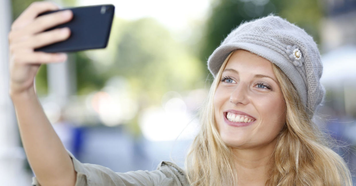 A young woman smiles as she poses for a selfie.