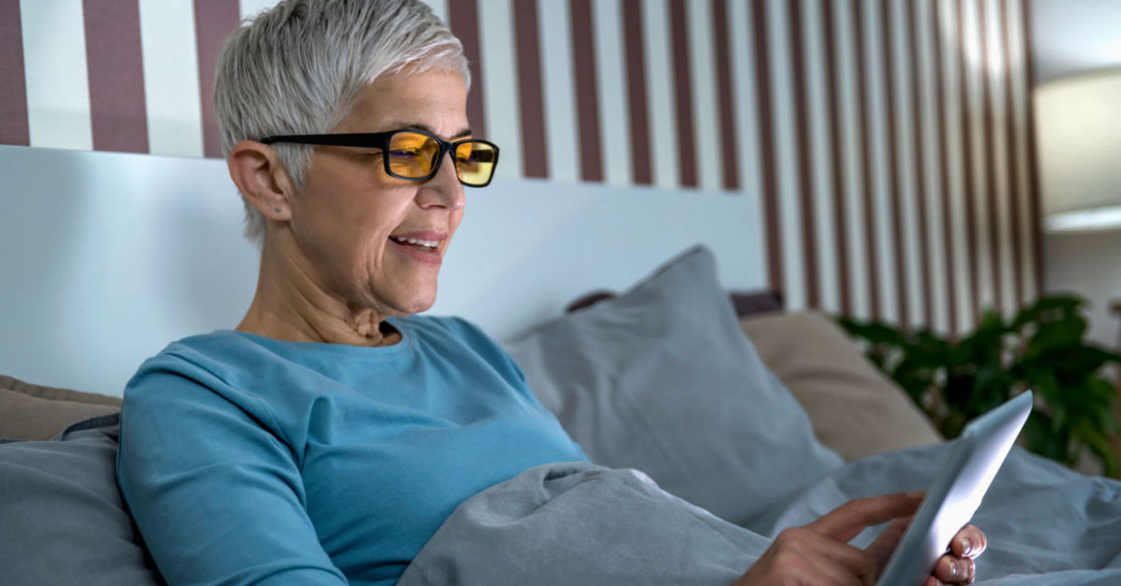 A woman wears blue light blocking glasses to look at her tablet.