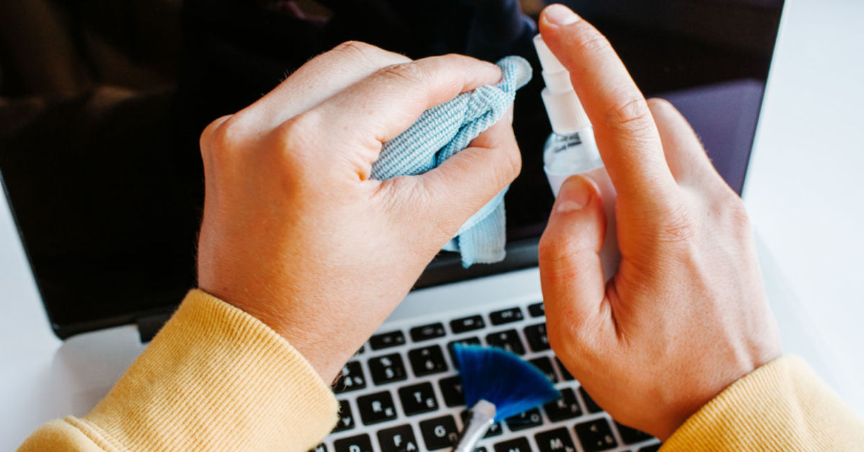 A man cleans his screen with spray and a cloth.