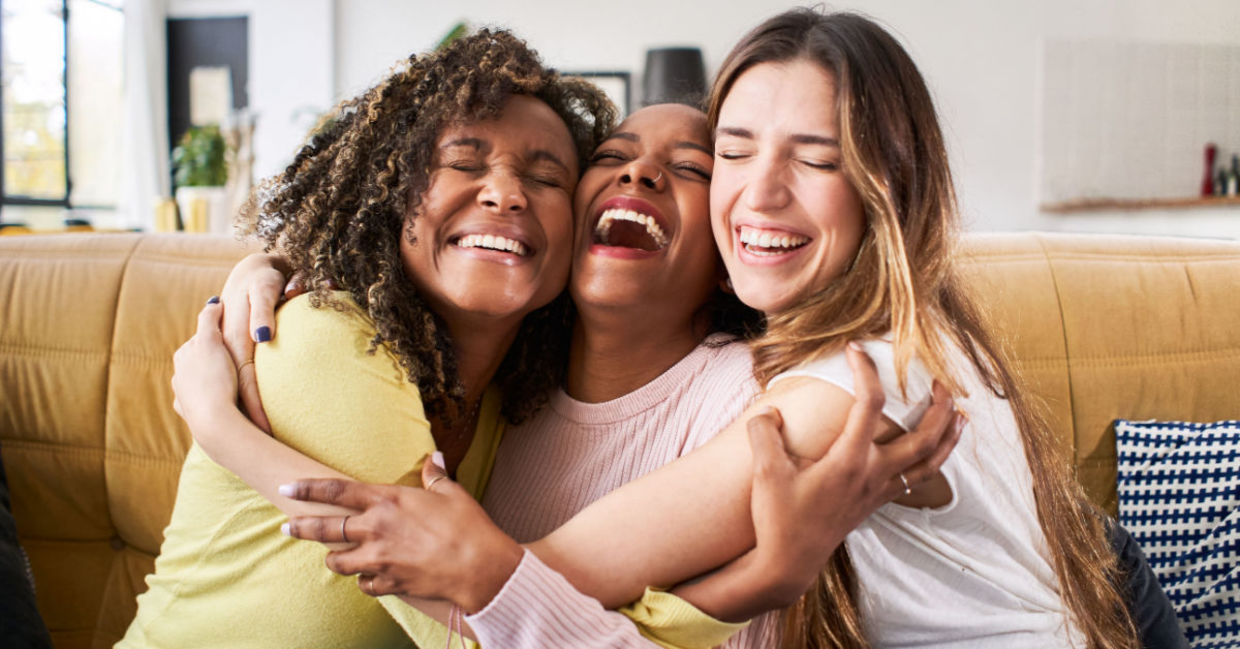 Three smiling friends enjoy a hug.