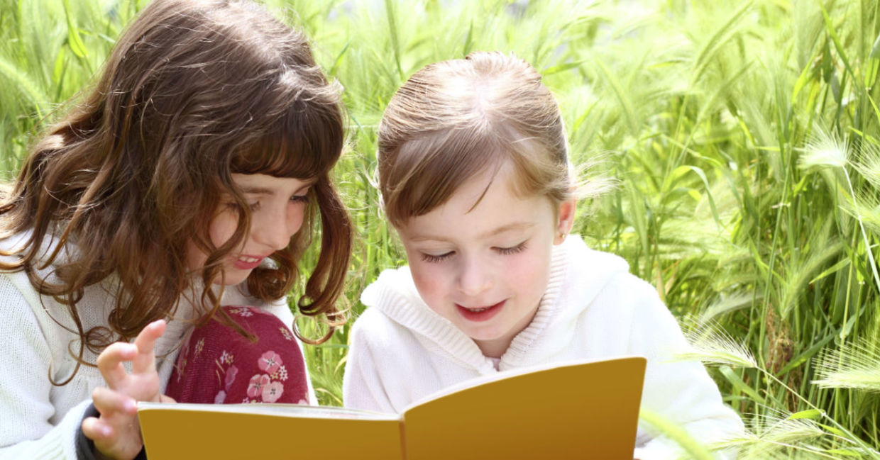 Two girls reading a book they found in a park.