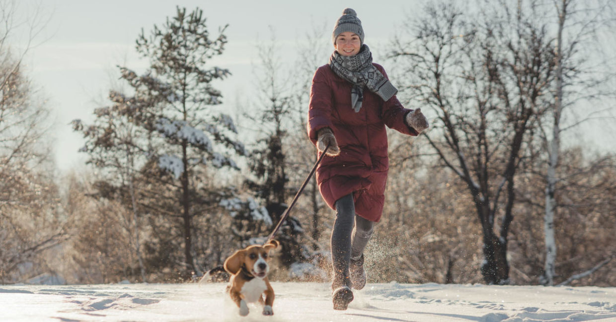 A woman running through snow in a forest is experiencing biophilia.