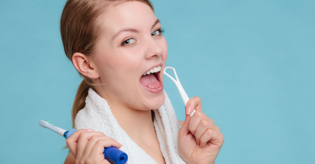 A woman with an electric toothbrush and tongue scraper.