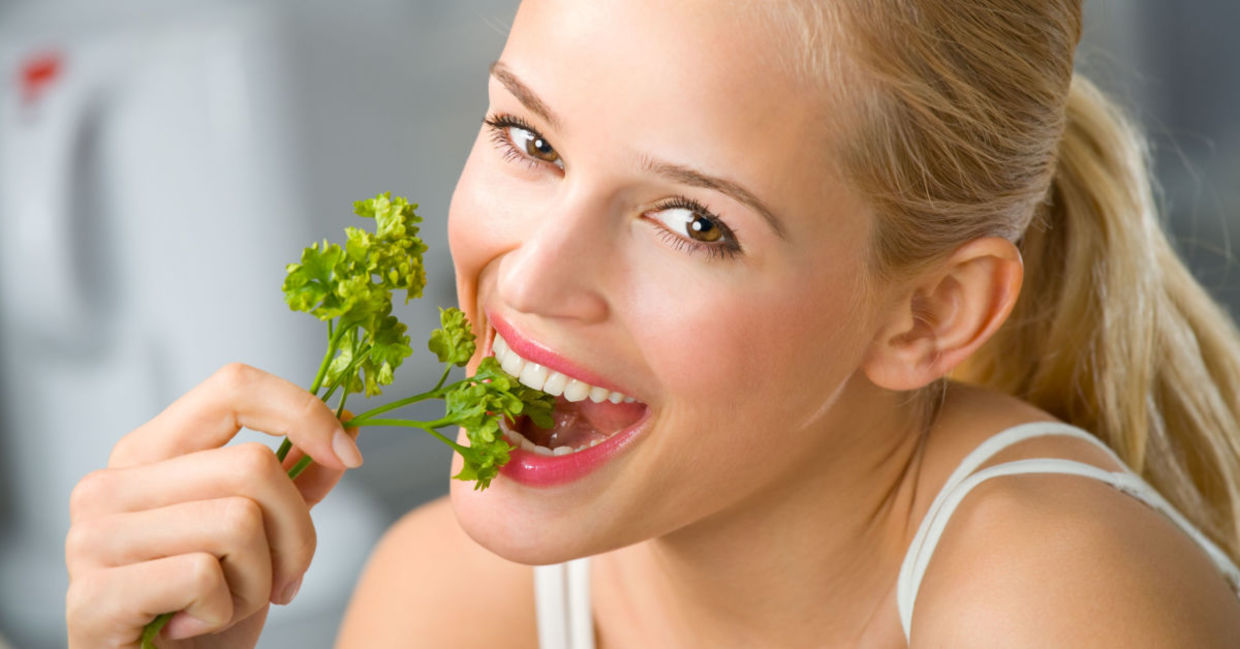 A woman eats a sprig of parsley.