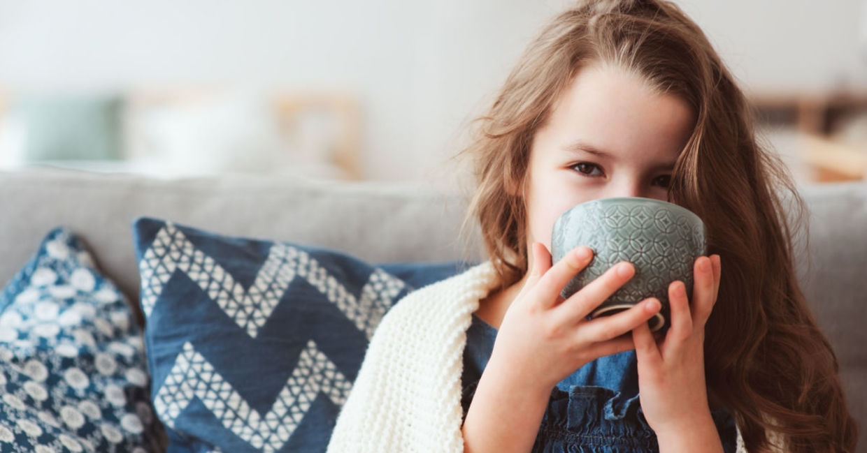 A young girl with the flu sips a hot drink.