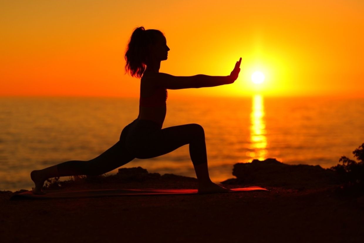 A woman does Tai Chi at sunset on the beach.