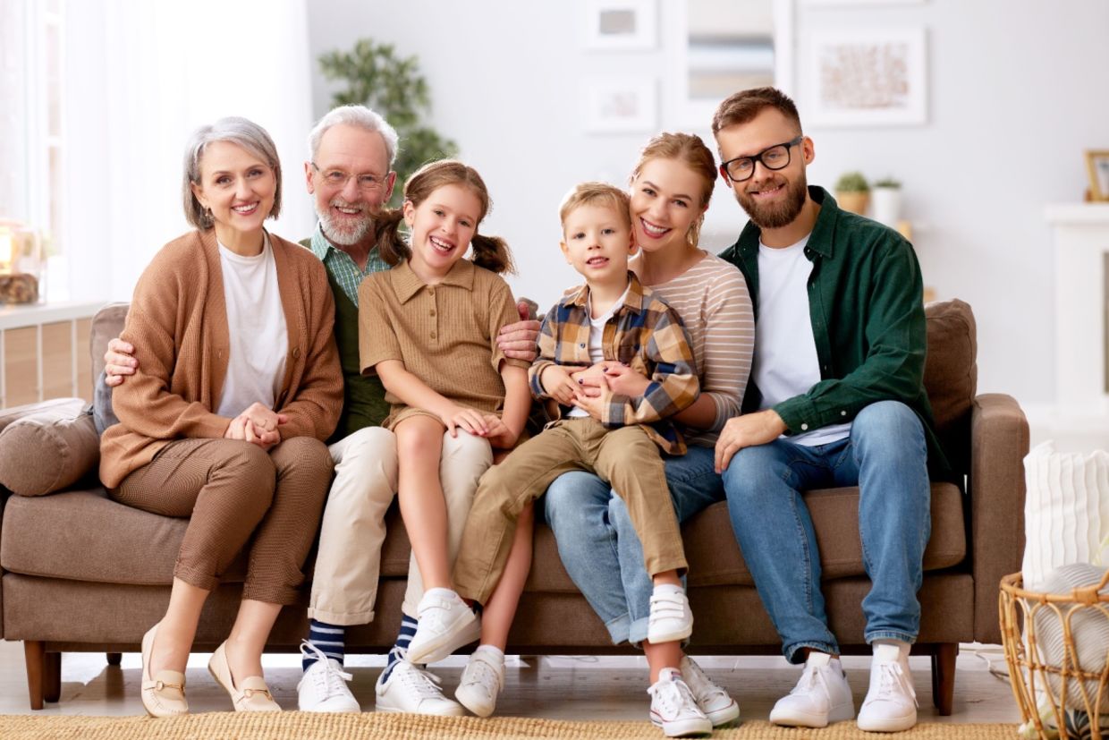 A family smiles while sitting on a couch.