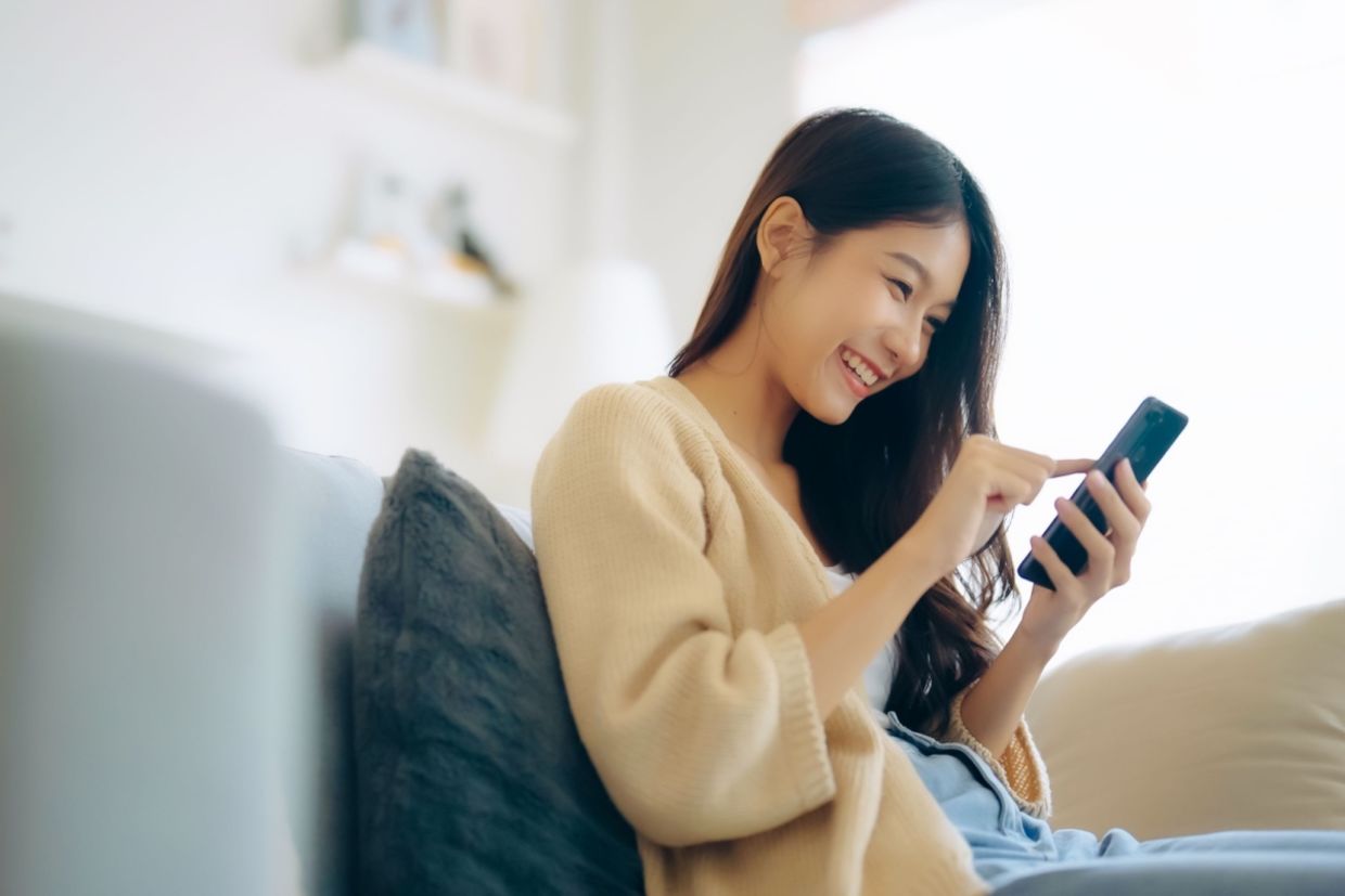 A woman sits on the couch using her phone.