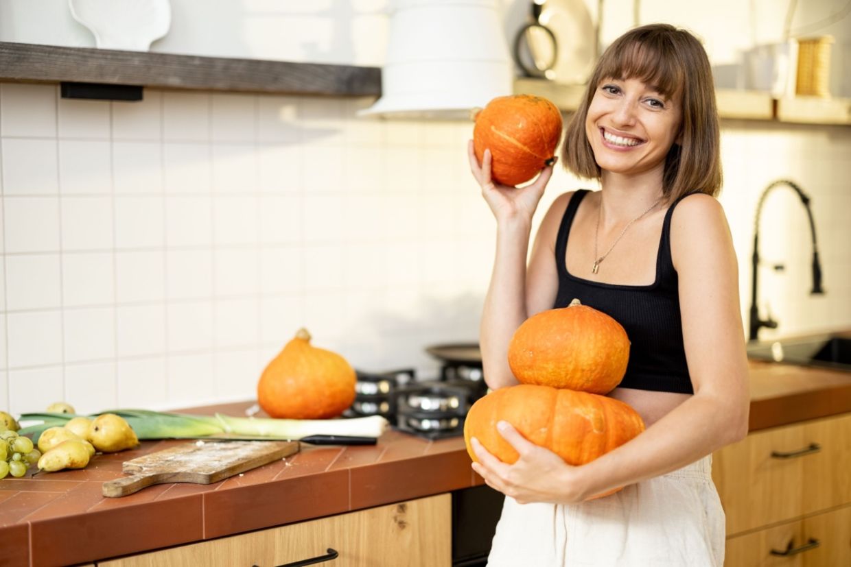 A woman holds pumpkins while preparing food in a kitchen.