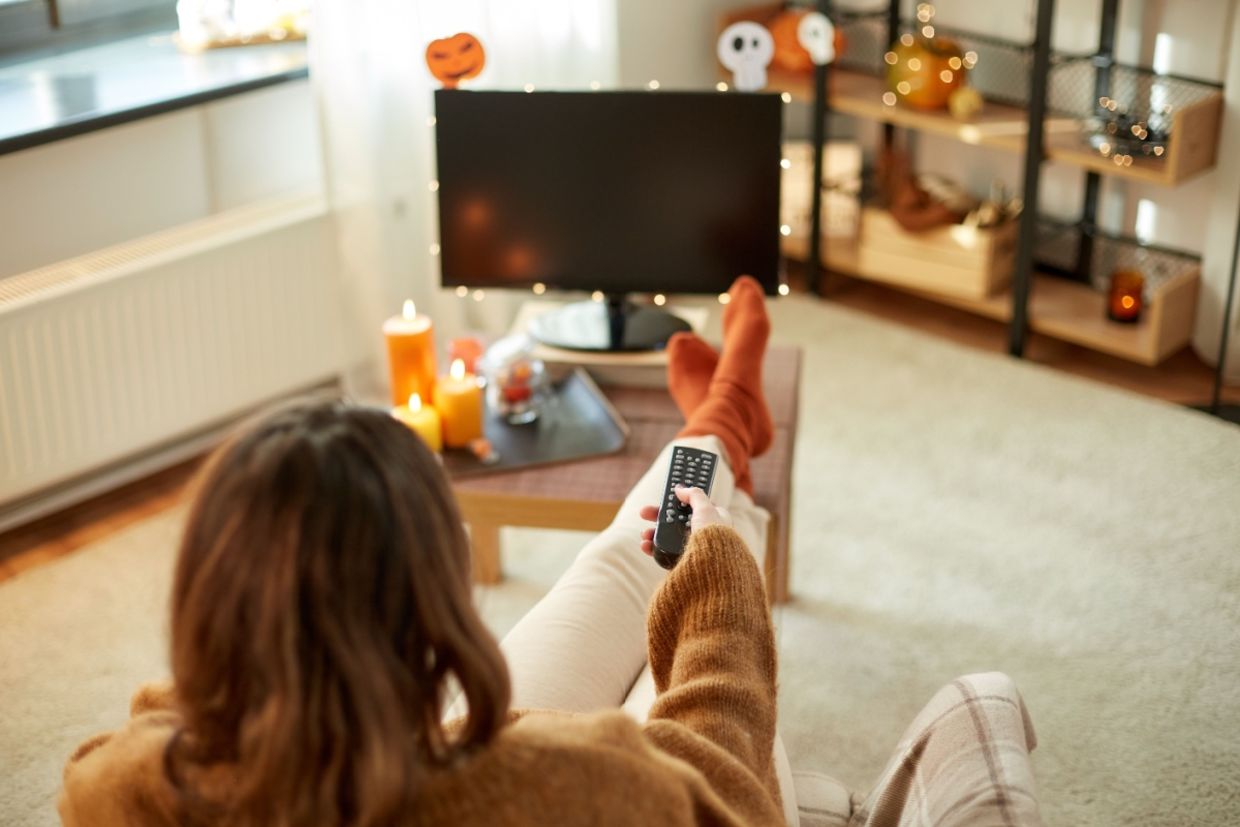 A woman holds a remote control and looks at a television.
