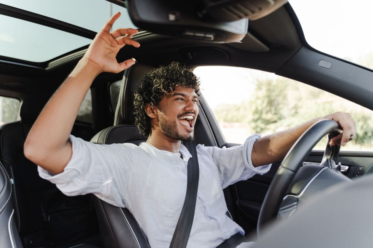A young man happily drives while singing to music.