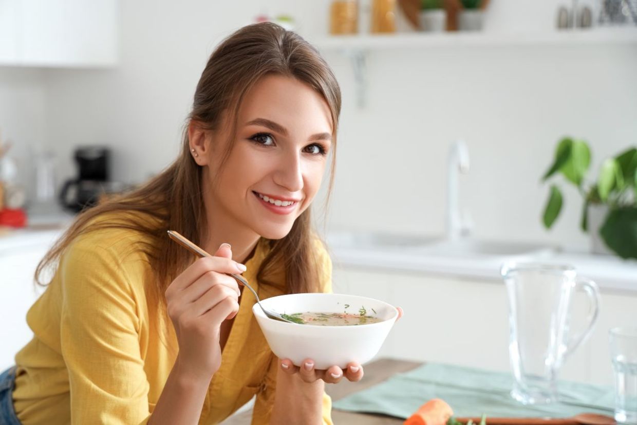 A woman eating hot chicken soup.
