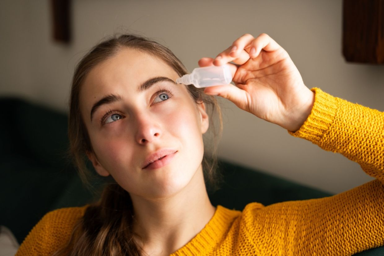 A woman using eye drops in a living room.