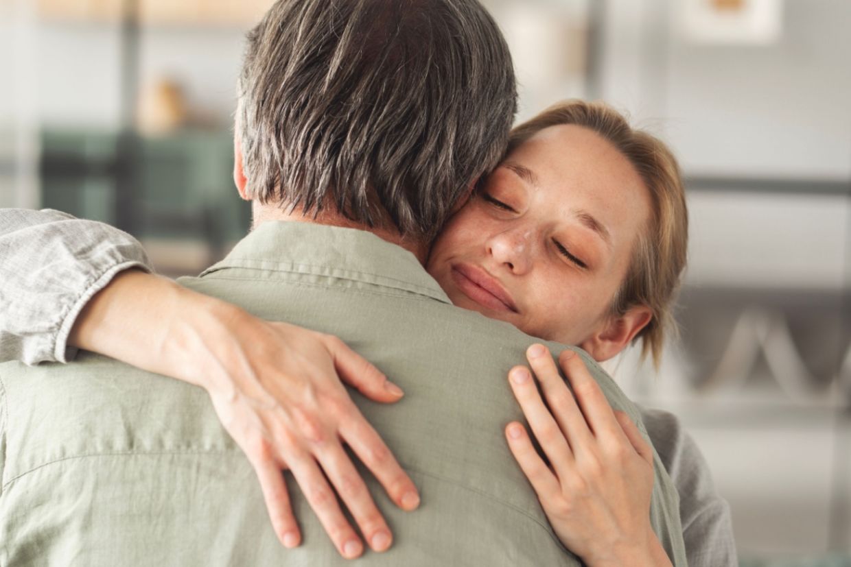 An adult daughter hugs her father.