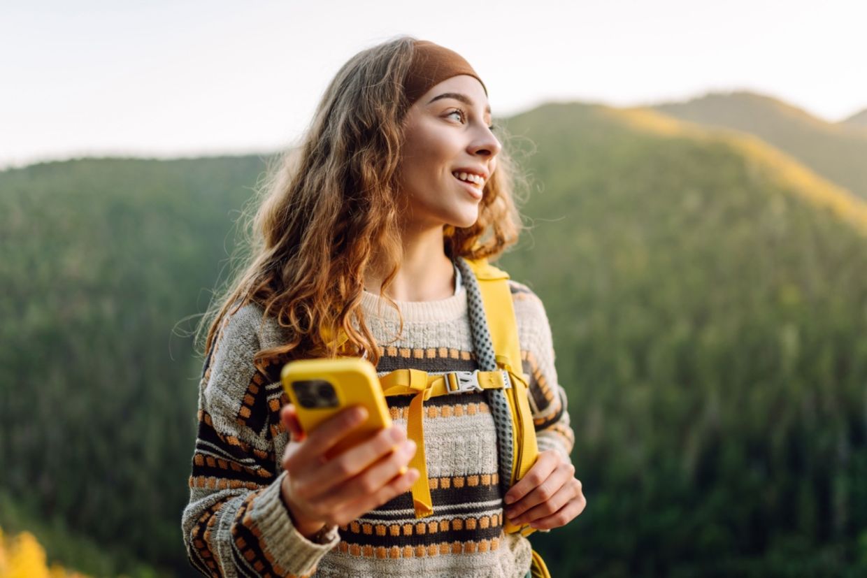 Alt: A woman walks in nature while holding her phone.