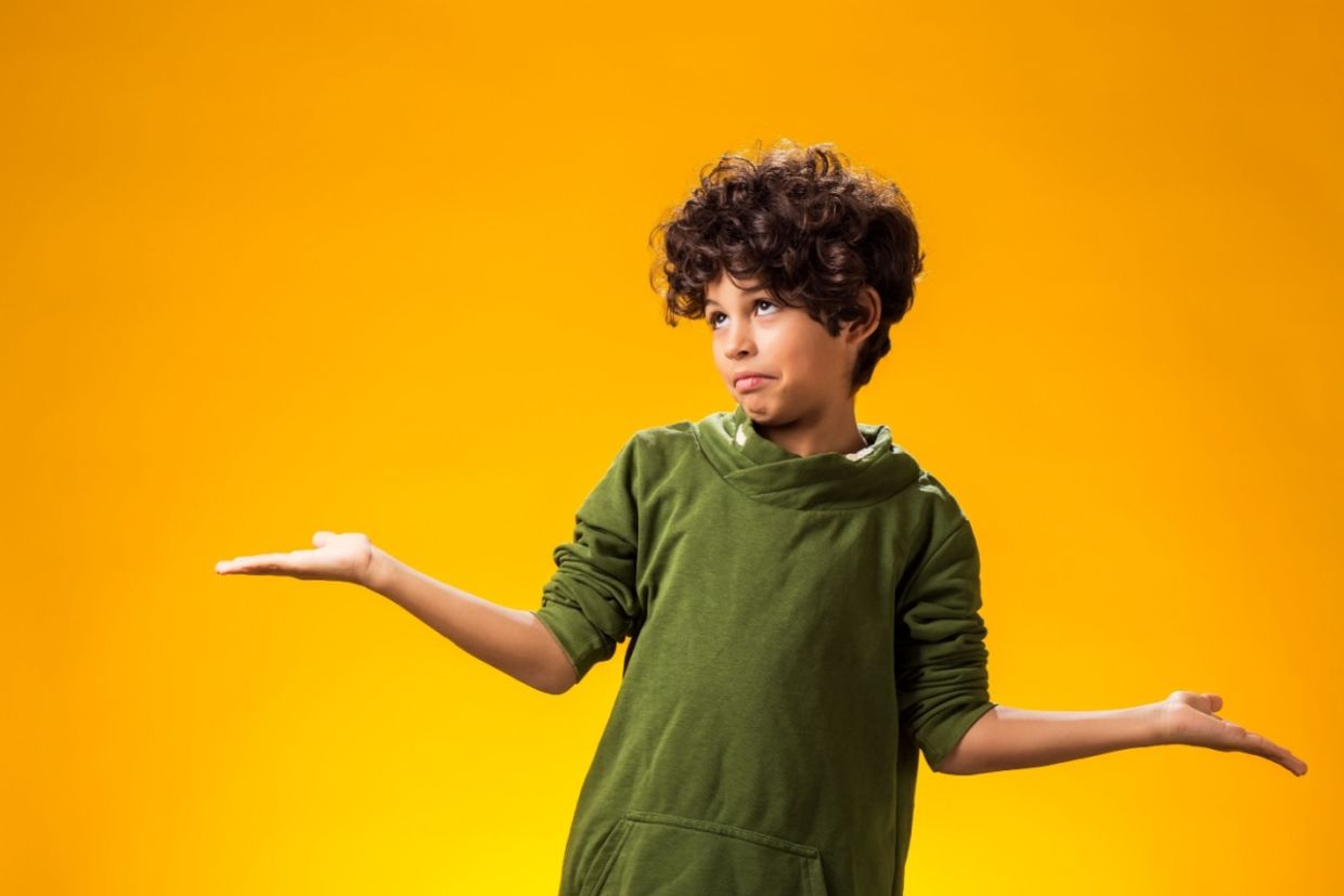 A boy keeps his arms to the side and shrugs.