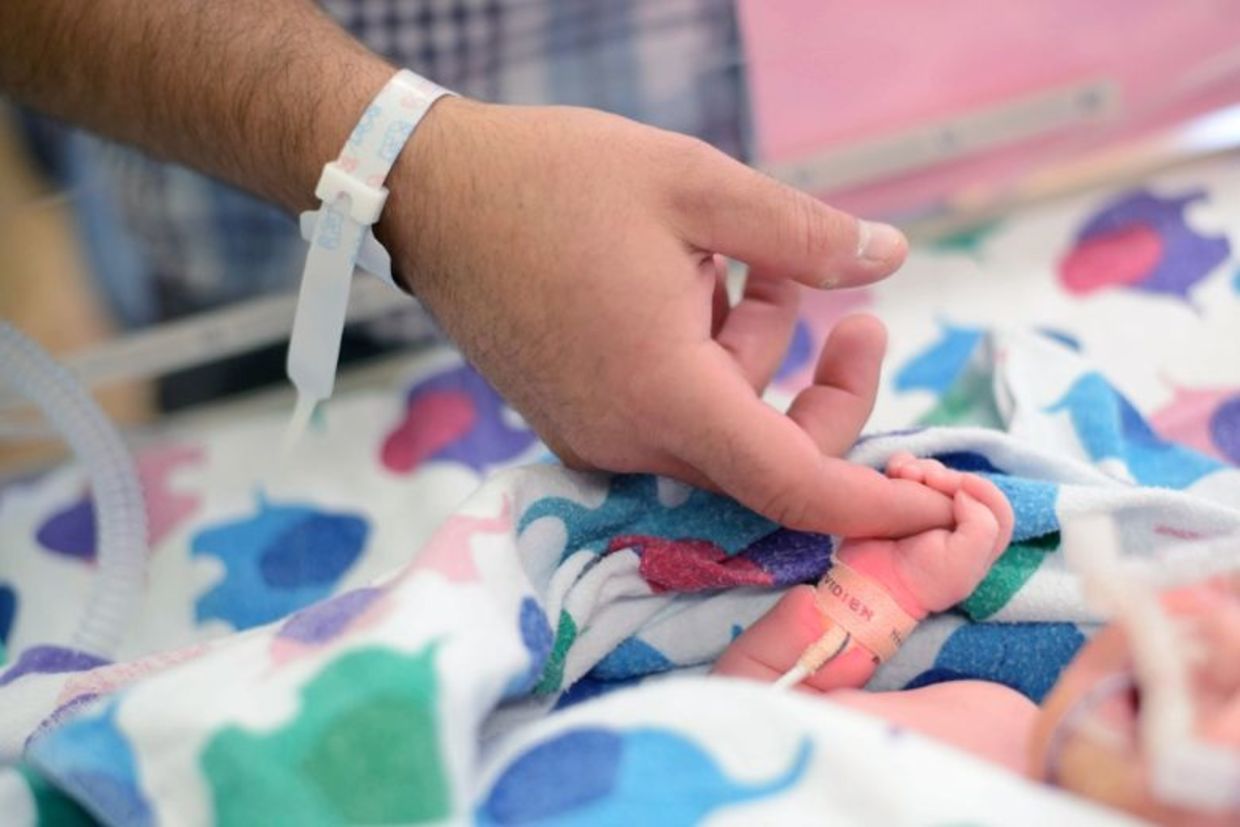 A first-time dad holds the tiny finger of his newborn who needed a little help breathing so was in the NICU.