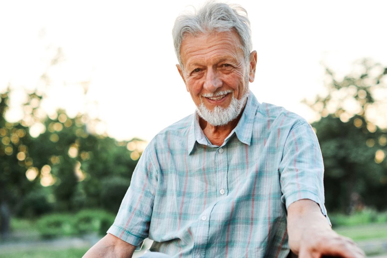 An elderly man smiling outdoors.