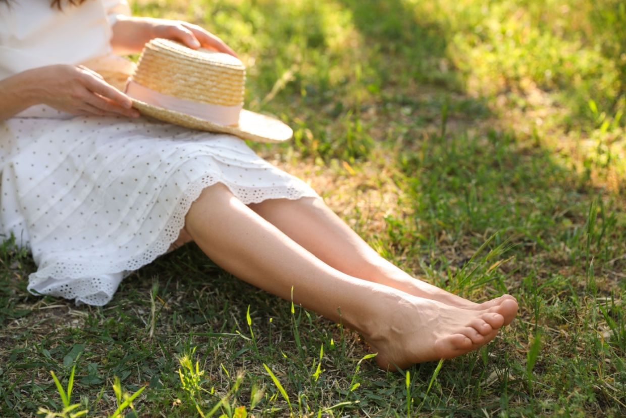 A woman sitting barefoot outdoors.