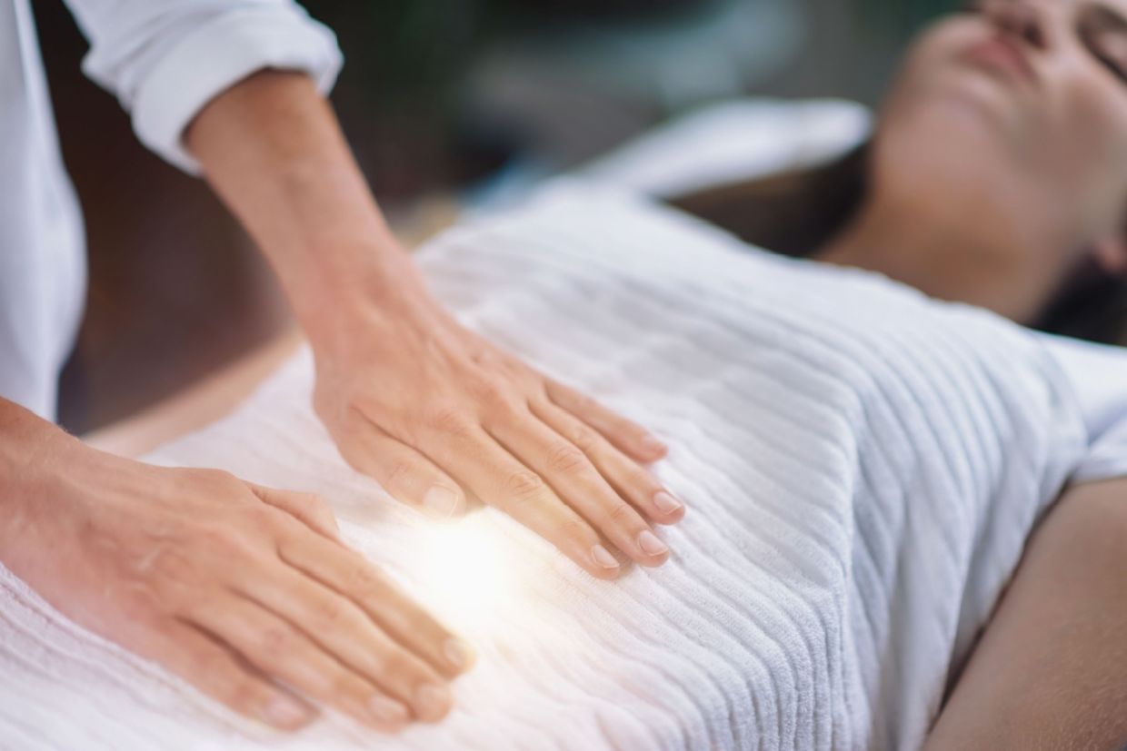 A woman during an energy healing session as a practitioner places hands gently on her upper body.