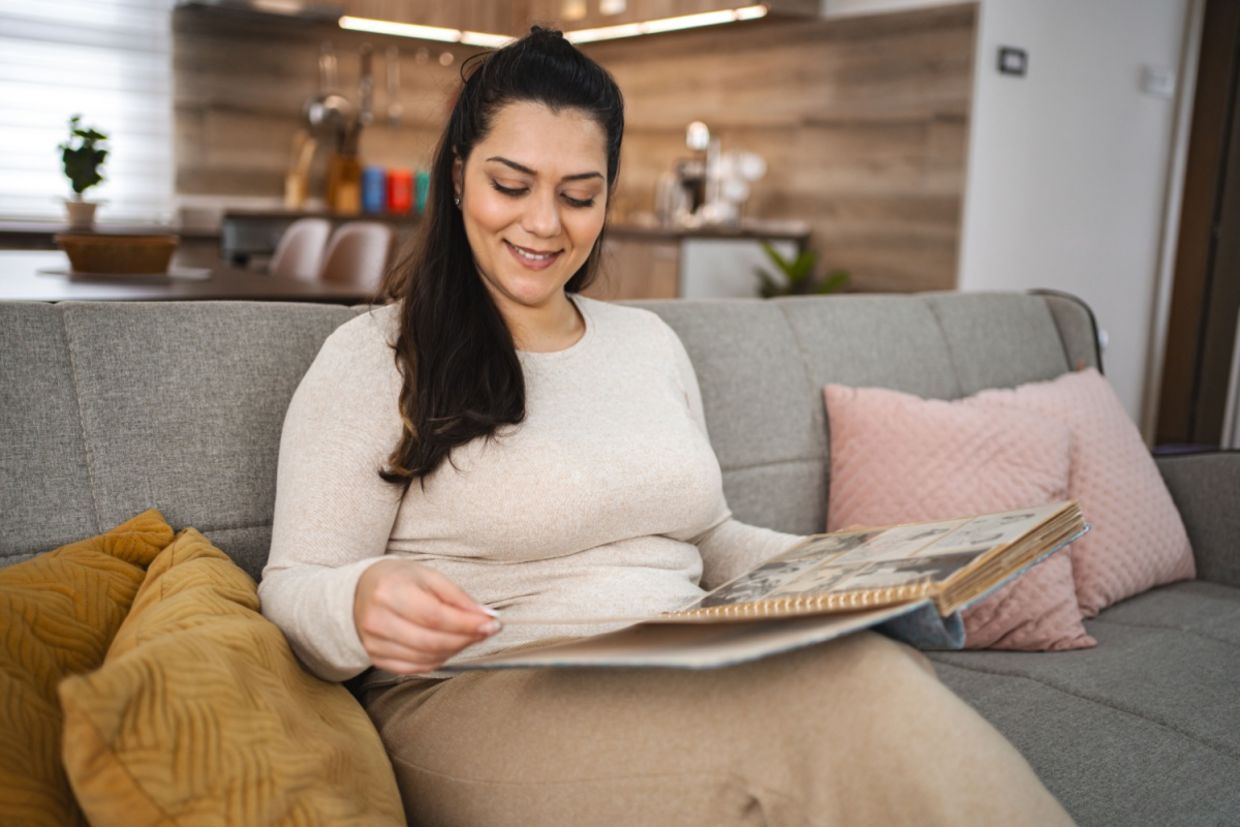 A woman looking at a photo album while sitting on a couch.