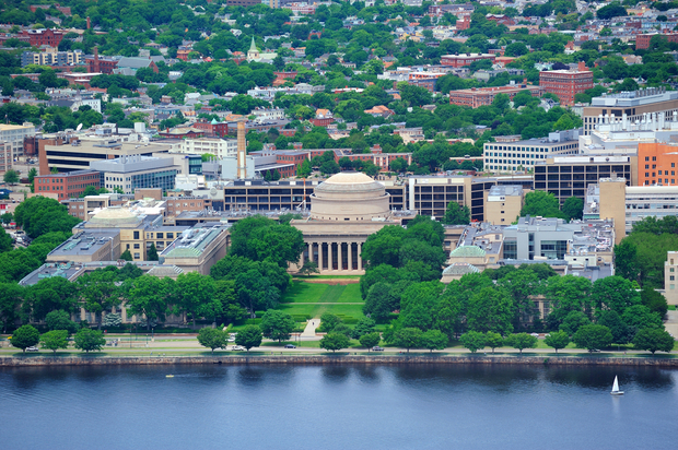 MIT MIT across the water, Aerial view of a white domed classical memorial building surrounded by government buildings and trees alongside a blue river with a sailboat, with residential areas on a hillside behind.