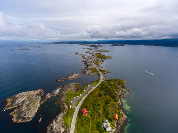 photo Aerial view of winding coastal road connecting small islands with red-roofed buildings surrounded by blue water and rocky terrain.