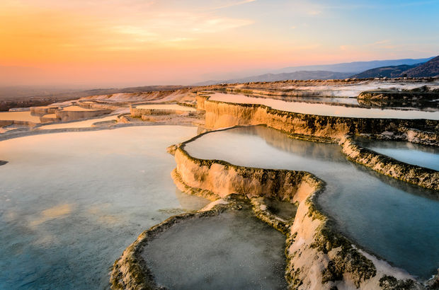 photo White limestone terraces with mineral pools filled with water, captured during golden hour with warm sunset lighting.