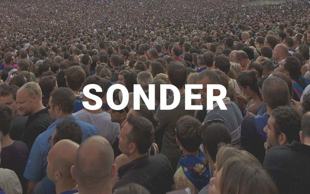 photo An aerial view of a massive, densely packed crowd of people with the word 'SONDER' displayed in large white capital letters across the center of the image.