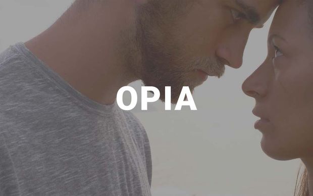 photo A close-up profile shot of a man and woman facing each other intimately, foreheads nearly touching, with the word 'OPIA' displayed in white capital letters in the center — a soft, muted-tone image.