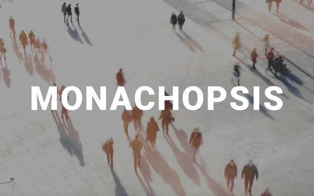 photo An aerial view of blurred figures walking across a pale urban plaza, casting long shadows, with the word 'MONACHOPSIS' displayed in large white capital letters across the center of the image.