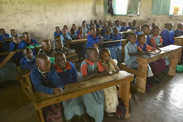 photo Large classroom full of African students wearing blue uniforms seated at wooden desks in a basic school building.