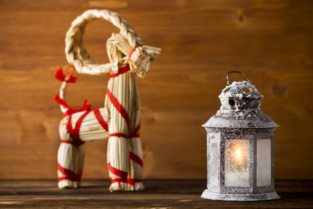 Straw Yule goat decoration with red ribbon and a frosted white lantern with glowing light on a wooden surface.