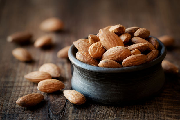 photo Raw whole almonds in a small dark blue ceramic bowl on a rustic wooden surface, with several almonds scattered beside the bowl.