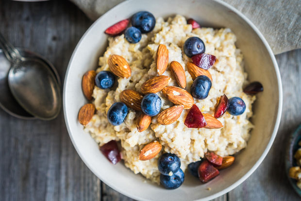 photo A bowl of creamy oatmeal topped with fresh blueberries, whole almonds, and sliced strawberries, viewed from above on a rustic wooden table with a silver spoon and linen napkin beside it.