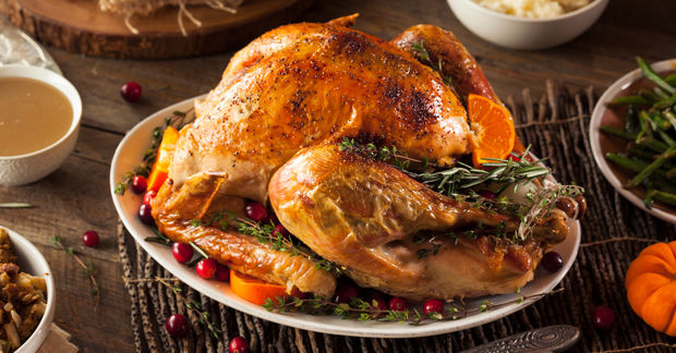 photo A golden roasted turkey garnished with rosemary, cranberries, and orange slices on a platter with side dishes nearby.