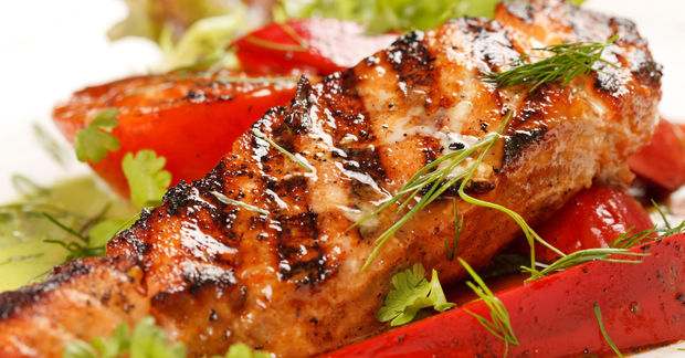 photo A grilled salmon fillet with charred grill marks, garnished with fresh dill and herbs, served with red peppers and greens.